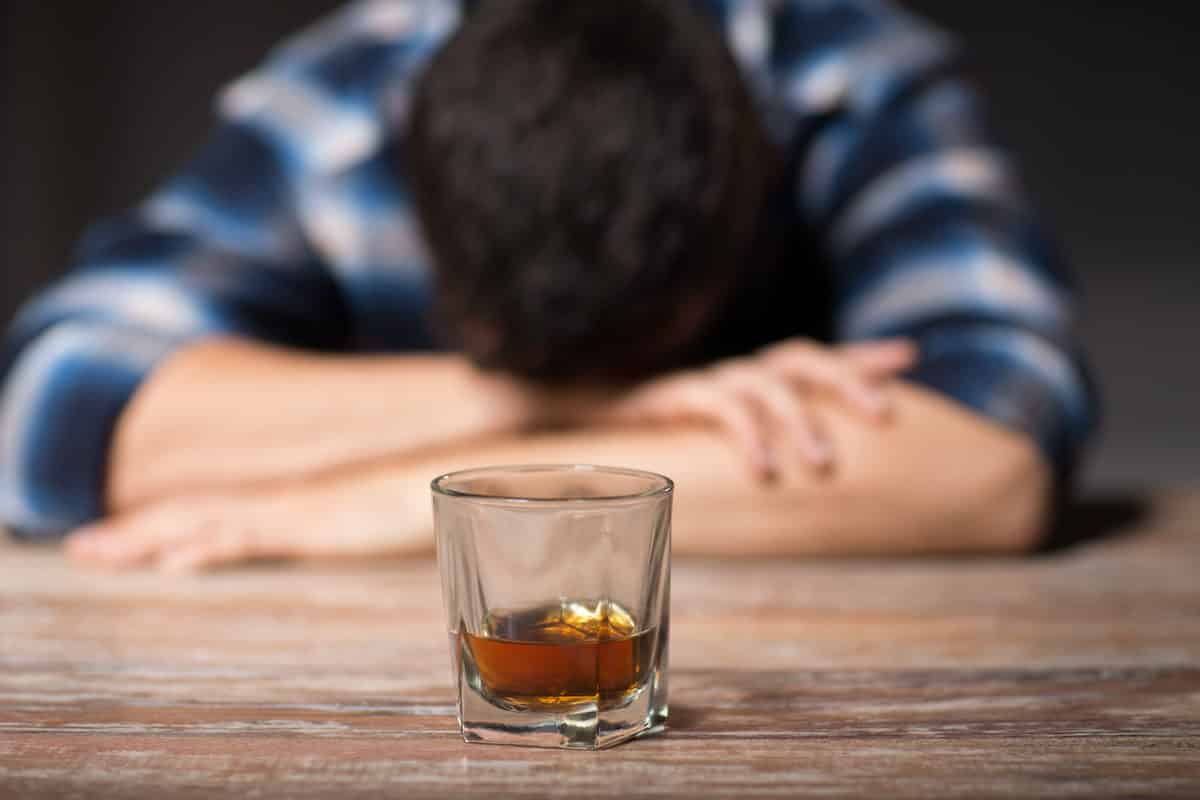 Hombre alcoholizado dormido sobre una mesa y con un vaso de licor