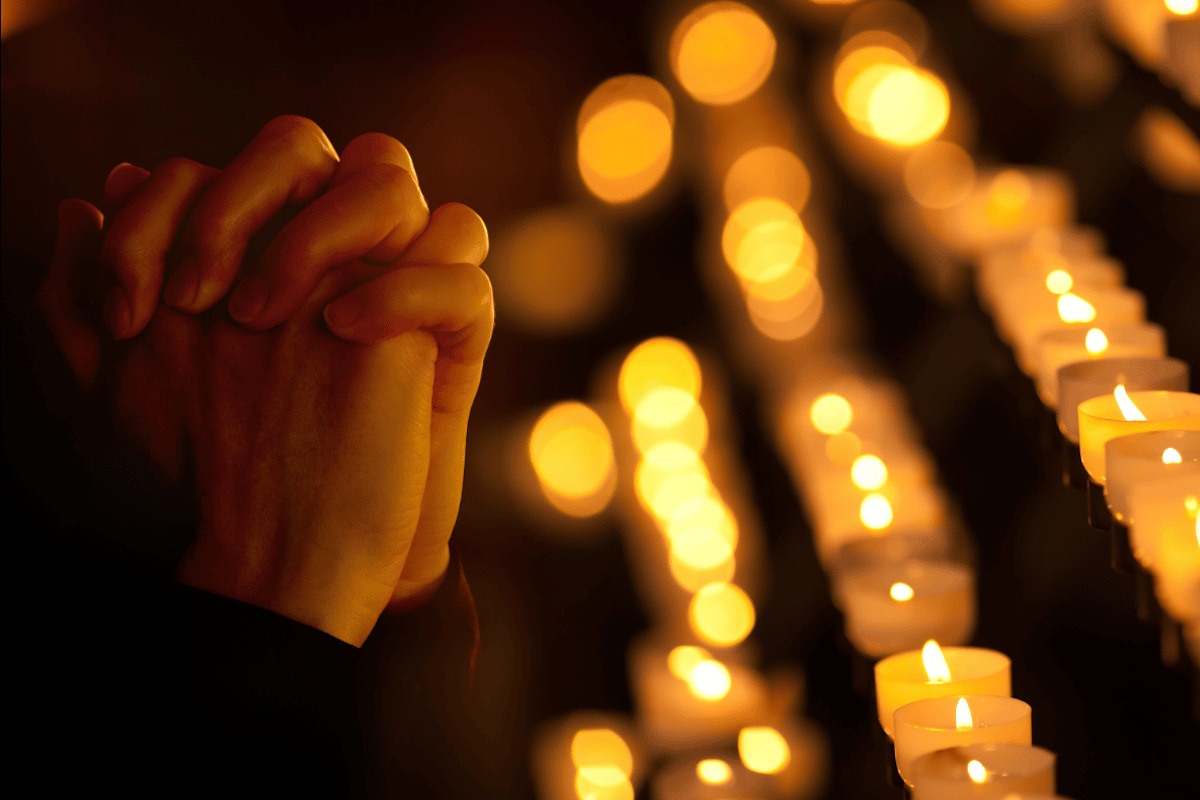 Veladoras encendidas y las manos de una persona rezando