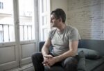 Hombre deprimido sentado en un sofá mirando hacia el exterior de su casa por una ventana / Foto: Especial