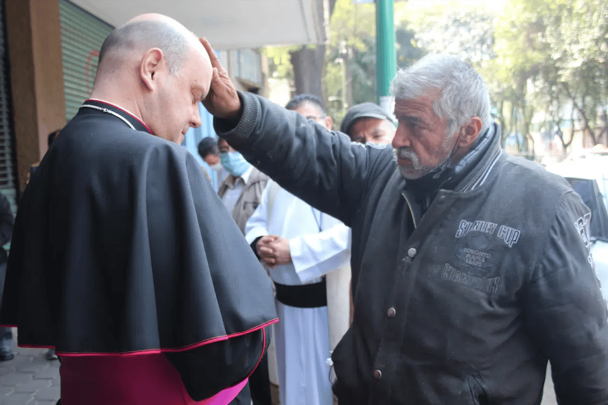 El obispo Francisco Javier Acero recibiendo la bendición de un indigente