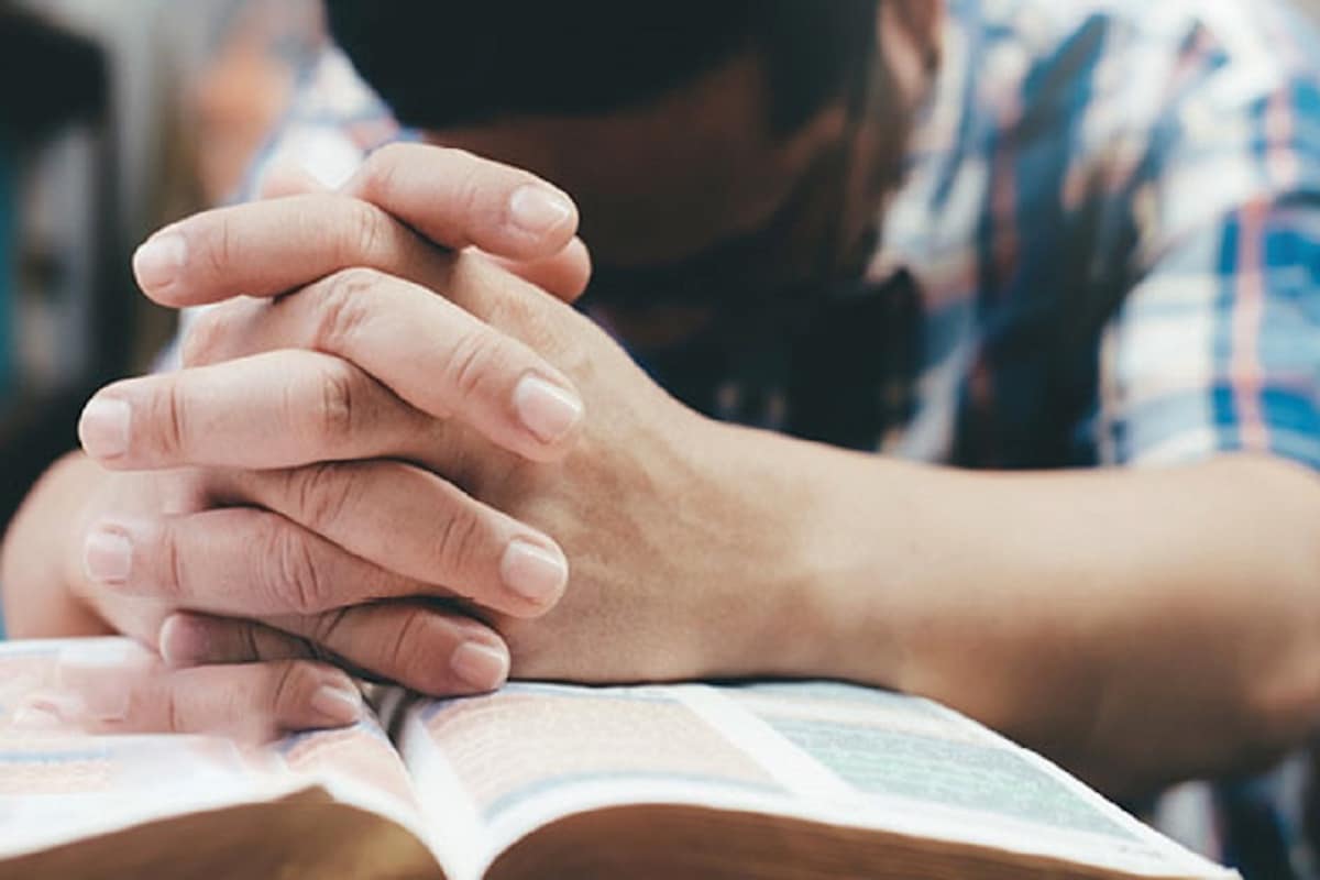 Hombre orando con las manos puestas sobre una biblia / Foto: Especial