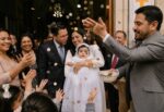 Un padrino lanza monedas durante la celebración de un Bautismo mientras familiares y niños participan con alegría a la salida de una iglesia, representando la tradicional costumbre del bolo.