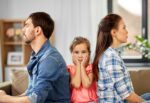 Niña triste entre sus padres distanciados tras un conflicto familiar por divorcio.